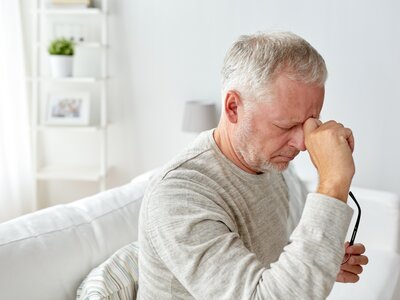 Älterer Mann sitzt auf einem Sofa und hält sich nachdenklich die Stirn | © PflegeBetreuer | unabhängige Pflegeberatung