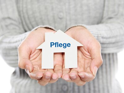 Hände halten ein kleines Haus mit der Aufschrift „Pflege“ – Symbol für Organisation der Pflege zu Hause und Entlastung im Alltag | © PflegeBetreuer | unabhängige Pflegeberatung