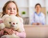 Kind mit Kuscheltier sitzt in einer Praxis während eine Fachkraft im Hintergrund sitzt | © PflegeBetreuer | unabhängige Pflegeberatung
